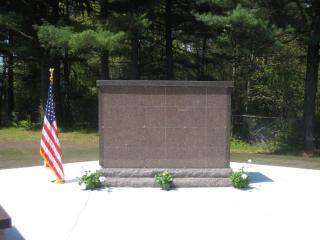 A granite columbarium with a U.S. flag and flowers, against a background of trees